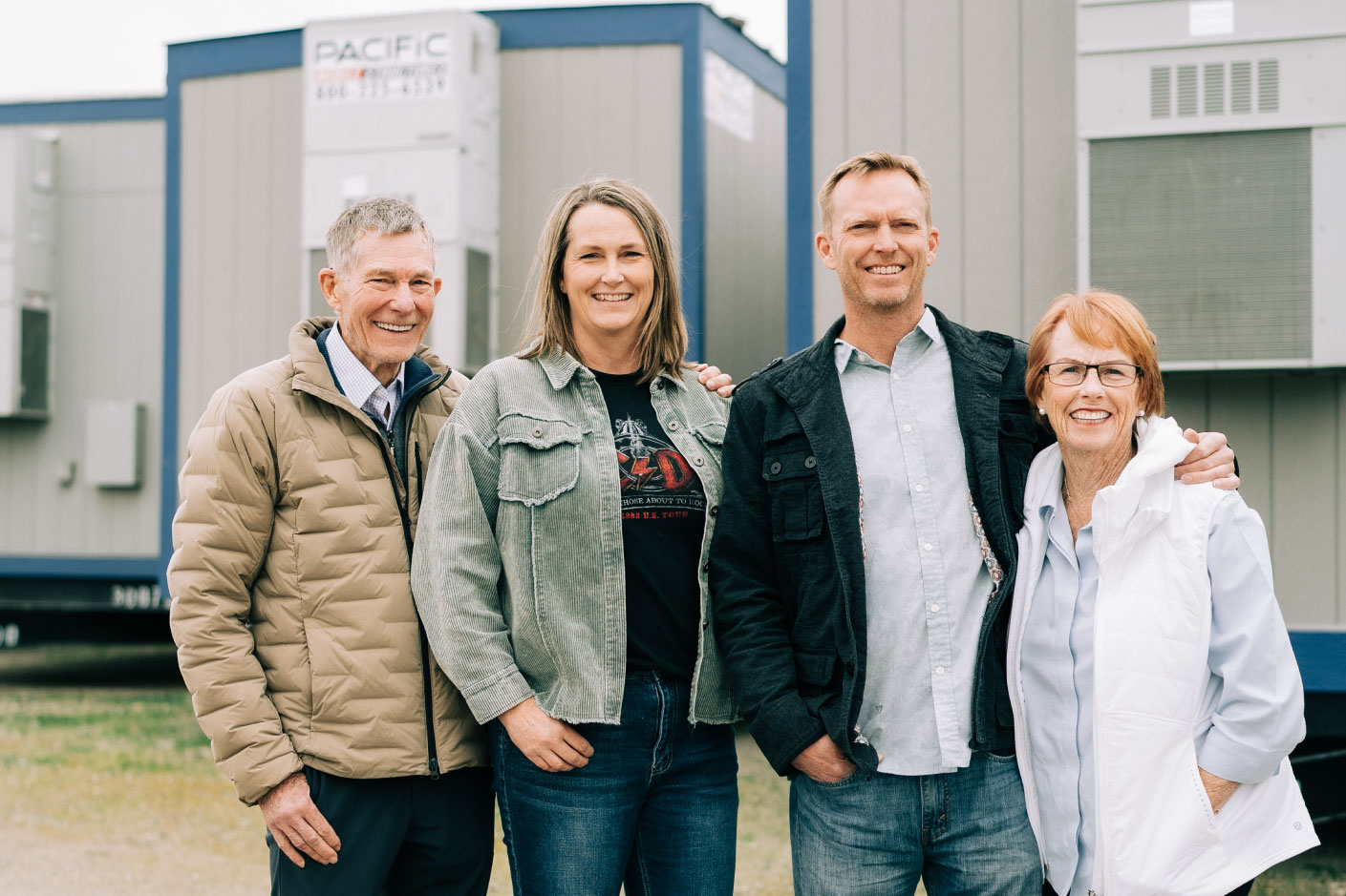 Pacific Mobile Structures family team smiles proudly in front of a modular building, representing their