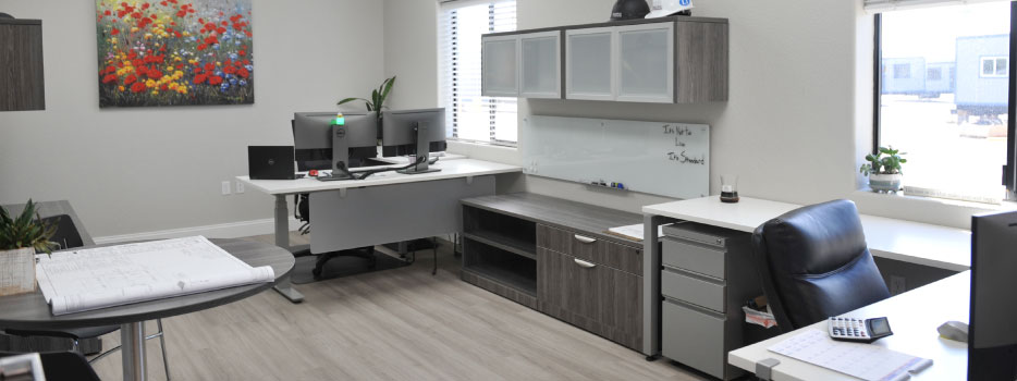 Modern office workspace with desks, computers, storage cabinets, and a whiteboard